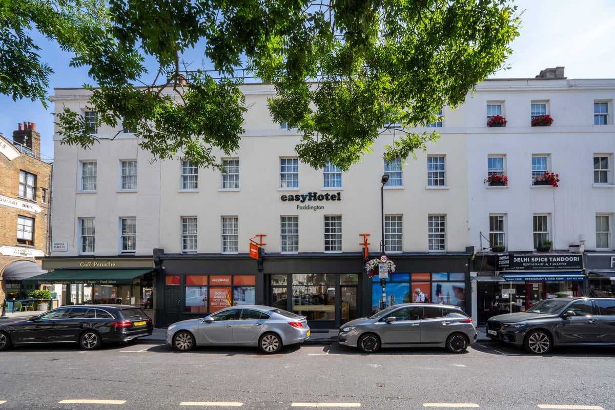 easyHotel Paddington, a white building with multiple windows, located on a city street with parked cars and surrounding shops.