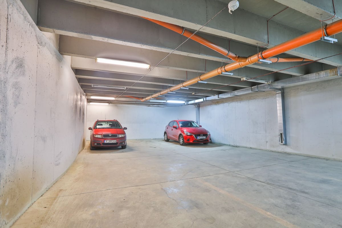 Underground parking garage at easyHotel Sofia with two red cars, concrete walls, and visible overhead pipes and fluorescent lighting.
