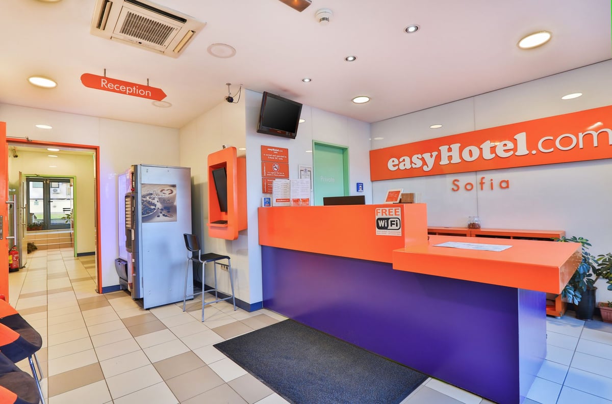 easyHotel Sofia reception area featuring a vibrant orange and purple desk, visible easyHotel.com Sofia branding, and a Free Wi-Fi sign.