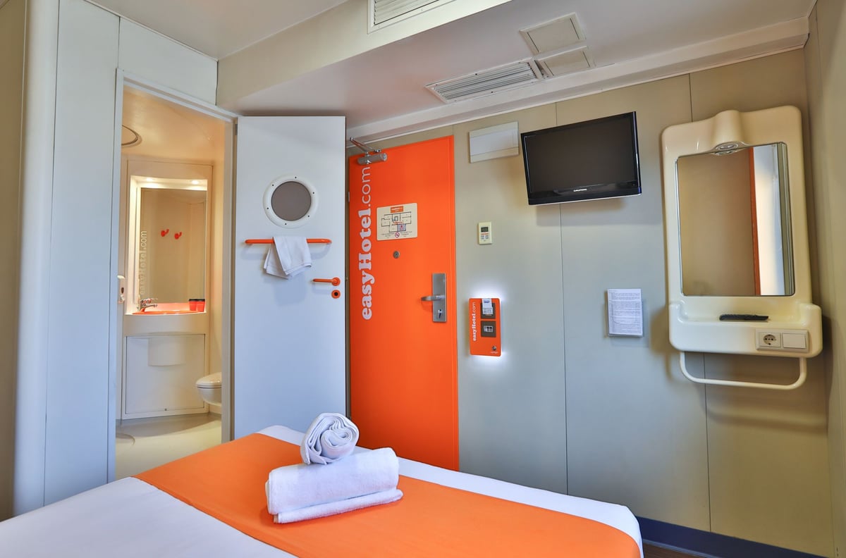 easyHotel Sofia Standard Double room with orange and white bedding, compact bathroom, TV, and orange entrance door.
