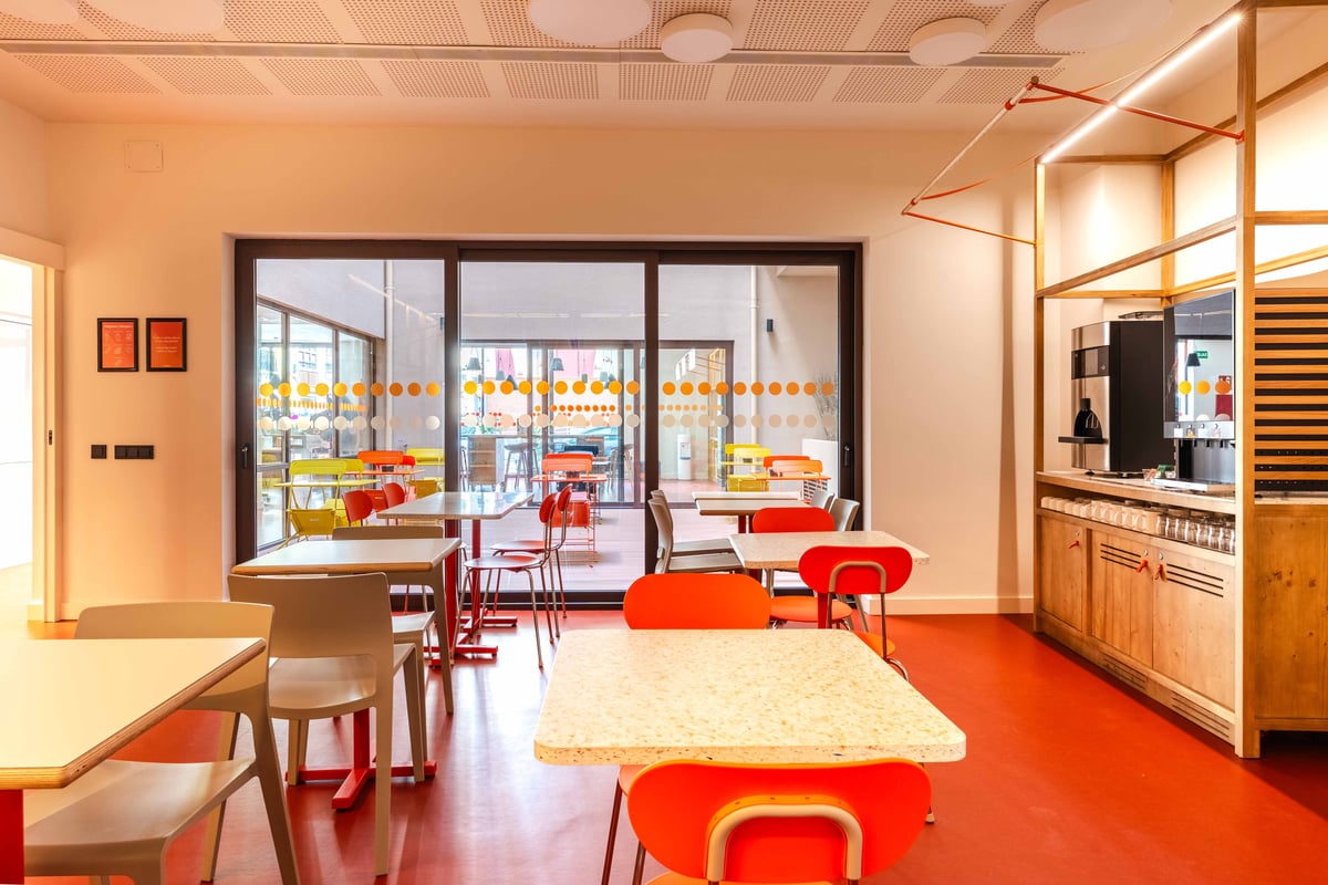 Bright red breakfast room with orange tables and chairs, featuring a window overlooking an outdoor seating area and a buffet service counter.
