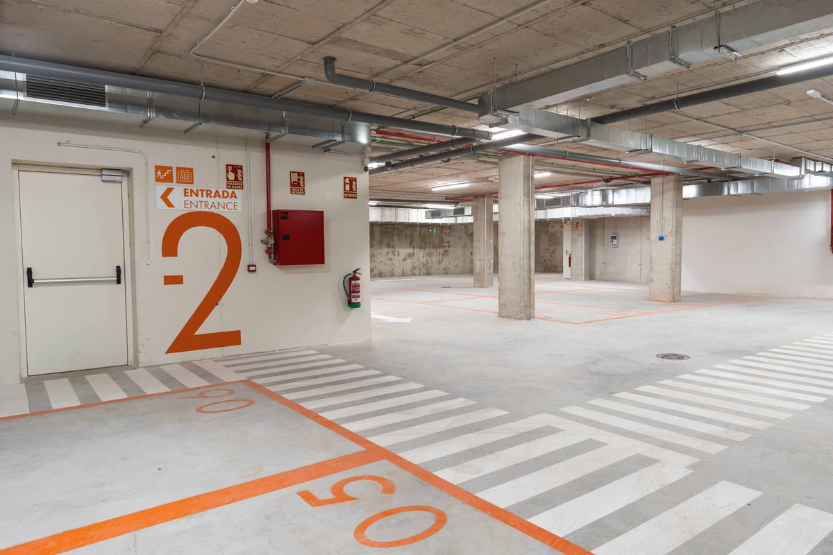 Car park interior with concrete floors, orange lane markings, and several parking spaces.