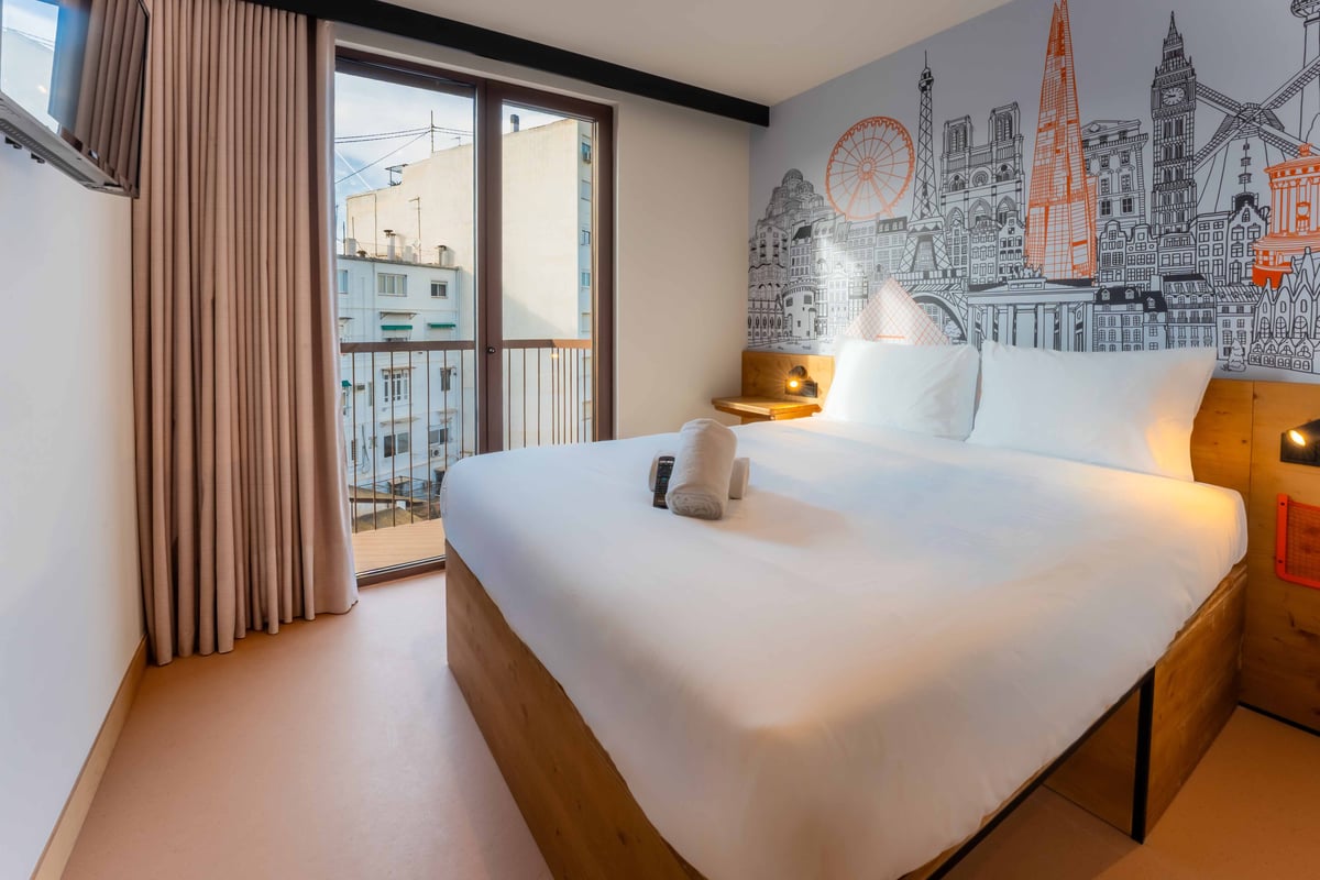 EasyHotel Valencia Ciutat Vella double room with double bed, white linens, and city skyline wallpaper.