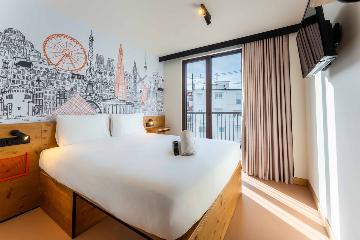 EasyHotel Valencia Ciutat Vella double room with white linens, pillows, and a city-themed mural.