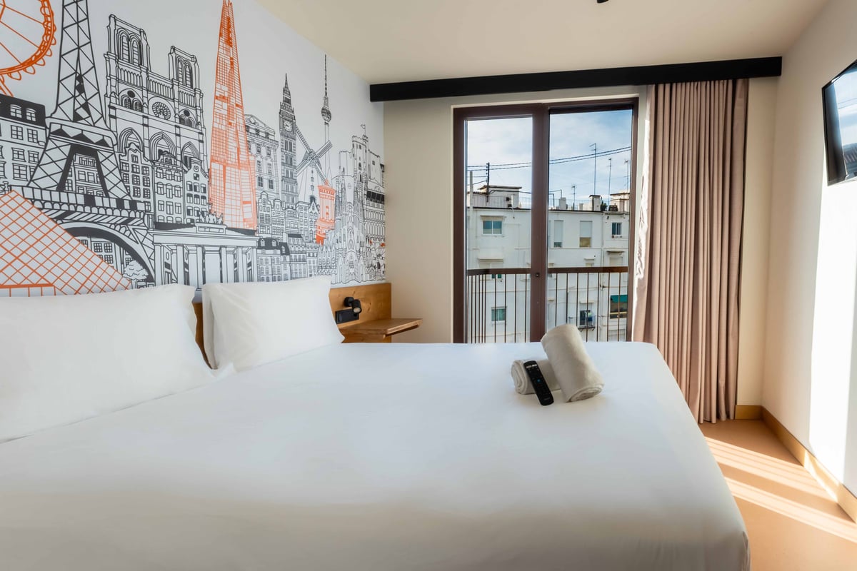 easyHotel Valencia Ciutat Vella double room with city skyline mural, bed, and balcony view.
