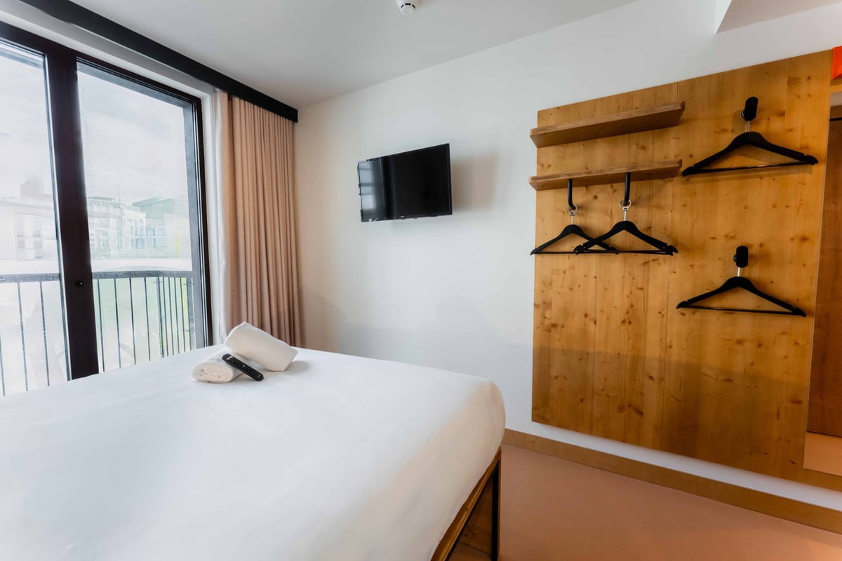 EasyHotel Valencia Ciutat Vella double room with white linens, a wall-mounted TV, and wooden hangers.