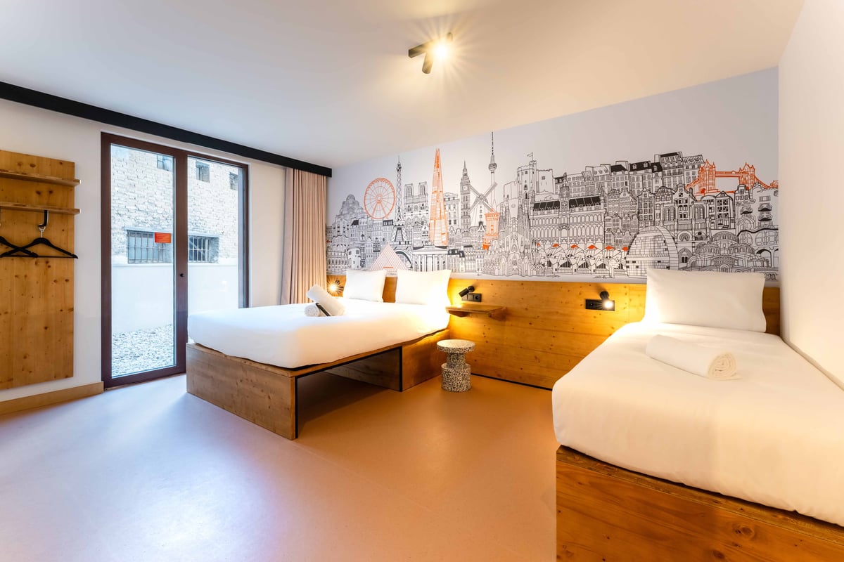 EasyHotel Valencia Ciutat Vella family room with two single beds, wooden headboard, and city-themed wallpaper.