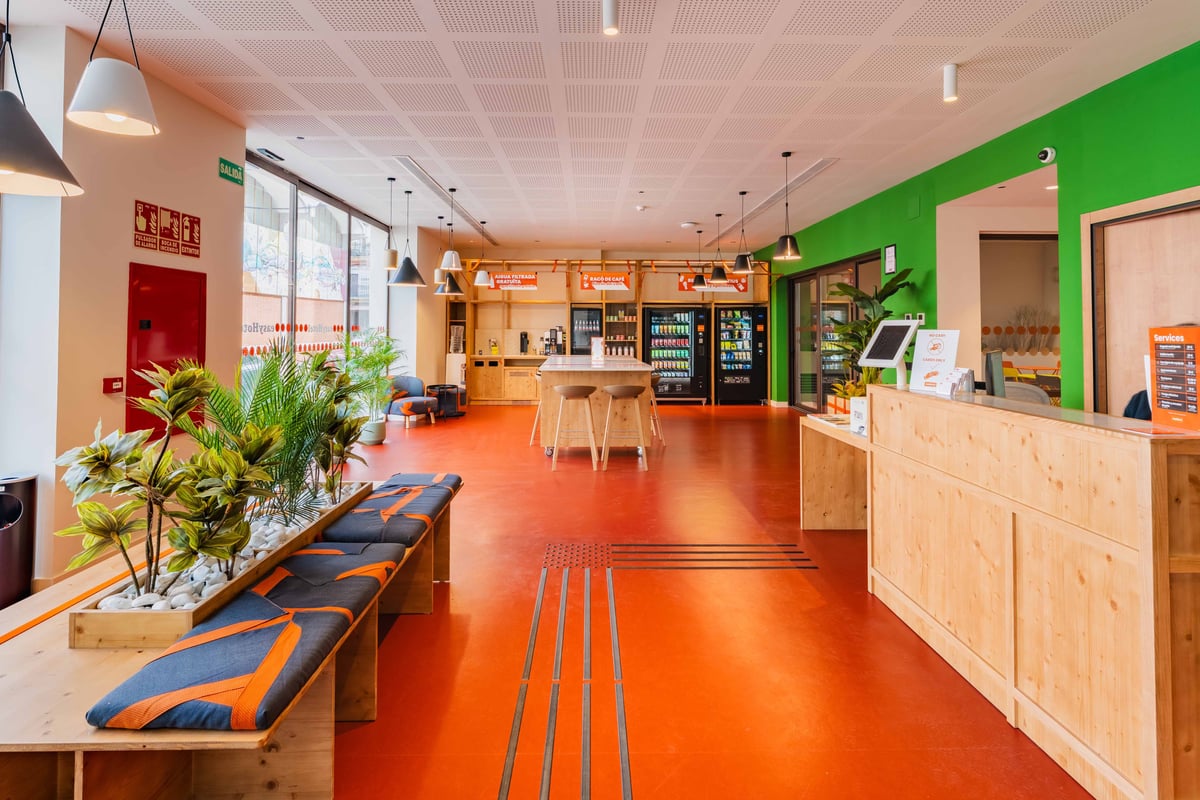 Bright reception area with orange and green accents, wooden benches, and a reception desk in Valencia, Spain.