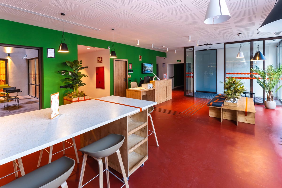 Bright green wall, wooden reception desk, and orange flooring in a Valencia city center lobby area.