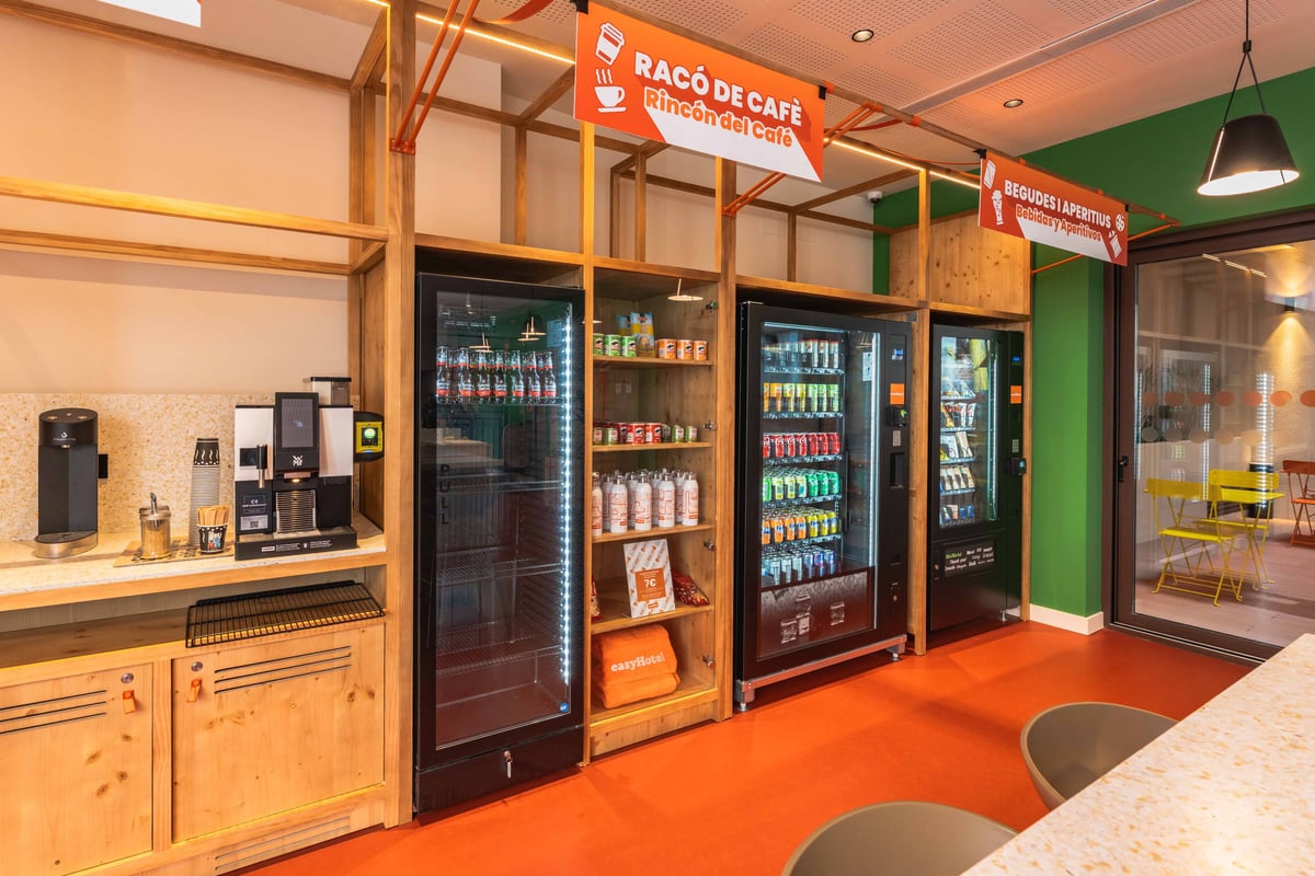 Modern reception area with vending machines and a coffee bar, featuring orange and white decor, located in Valencia, Spain.