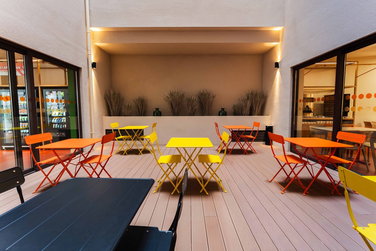 Valencia, Spain - Outdoor terrace seating area with bright yellow tables and red chairs, surrounded by a modern building structure.