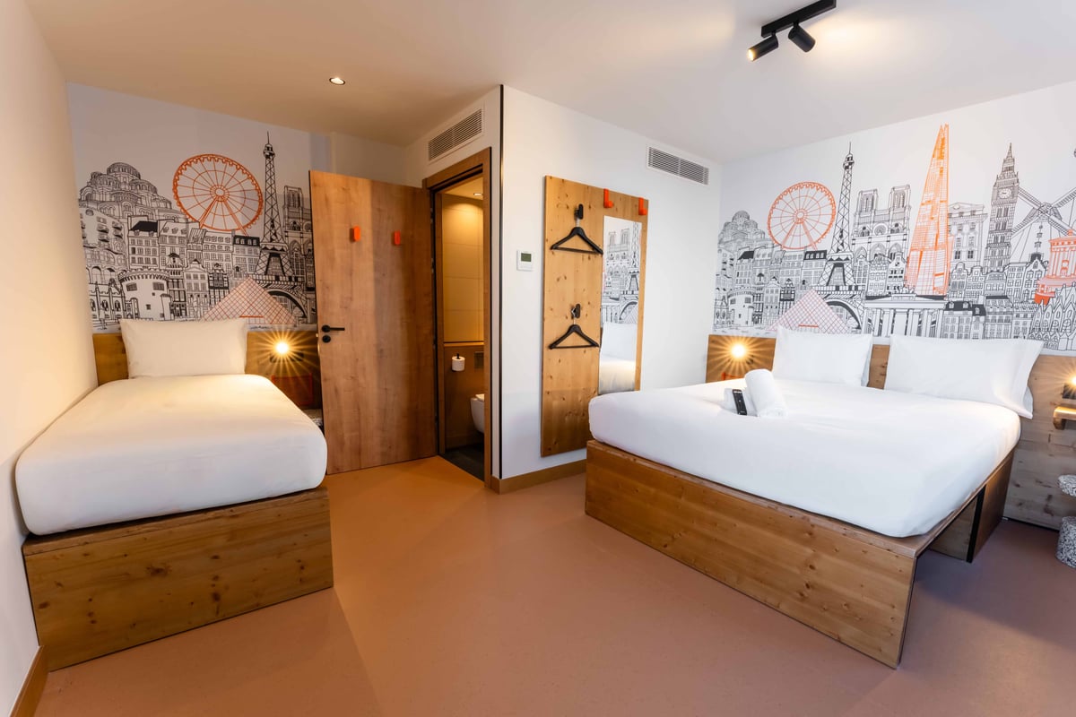 EasyHotel Valencia Ciutat Vella triple room with two single beds and one double bed, white linens, and city-themed wallpaper.