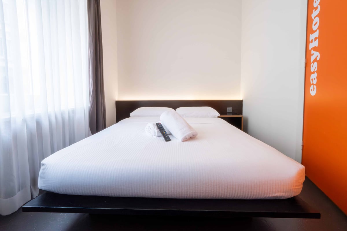 EasyHotel Zurich City Centre accessible double room with white linens, pillows, rolled towels, and a remote control.