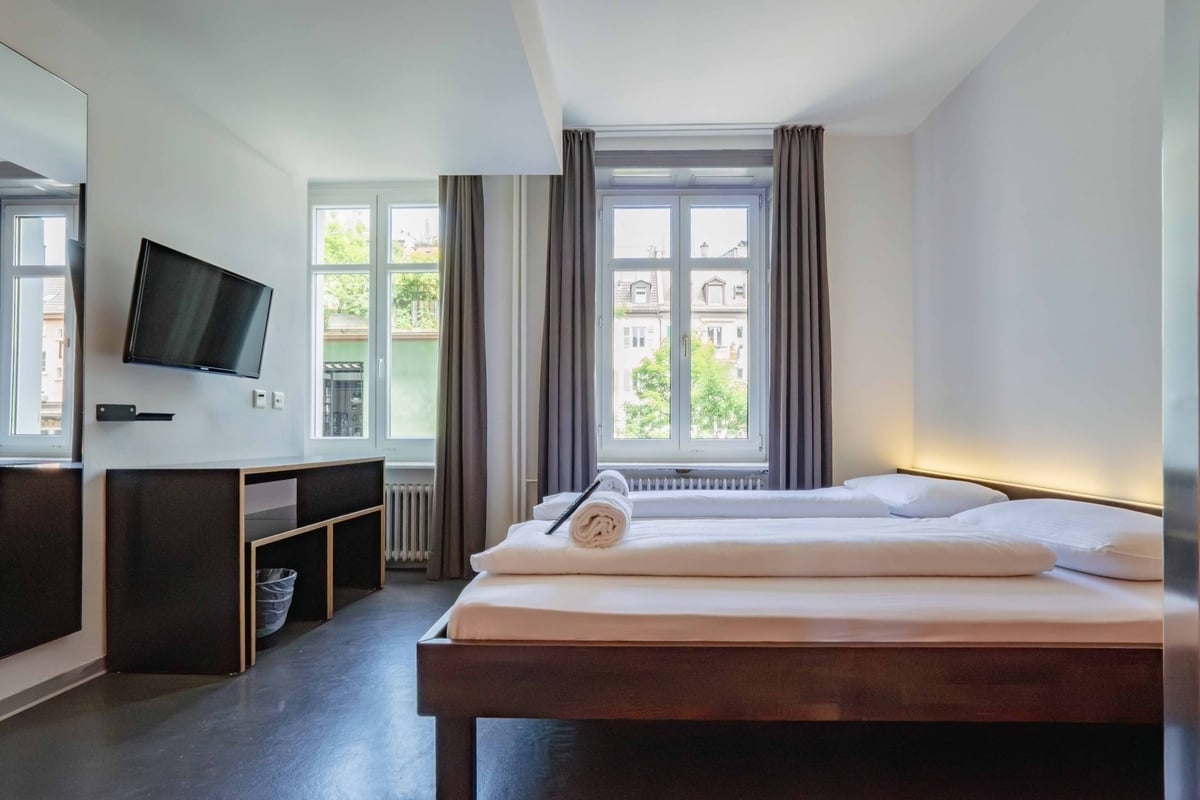 EasyHotel Zurich City Centre twin room with two single beds, white linens, and a dark wood frame. Window with grey curtains and view of city buildings.
