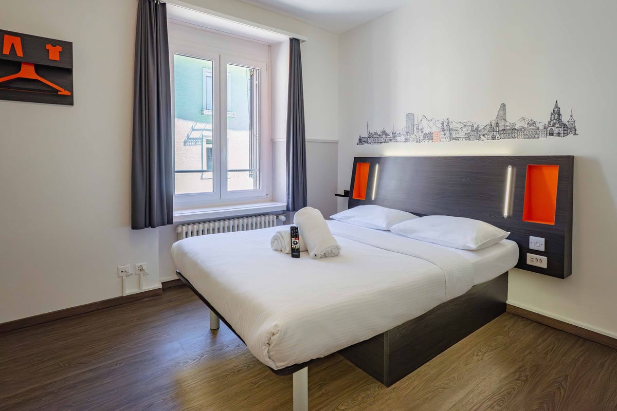 EasyHotel Zurich Limmatplatz double room with a bed, pillows, and a city skyline decal on the wall.