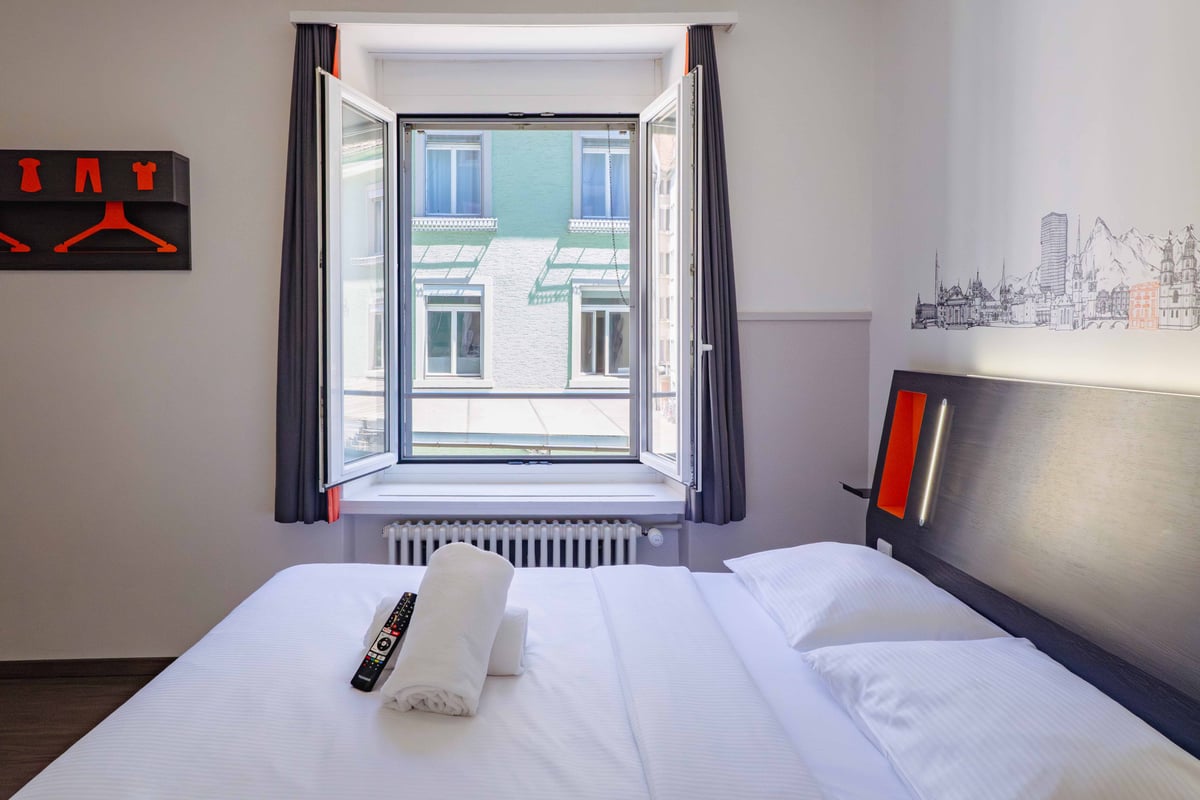 EasyHotel Zurich Limmatplatz double room with white linens, pillows, and a window overlooking a city street.