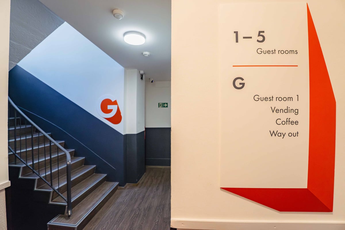 easyHotel Zurich Limmatplatz reception area with a sign indicating guest rooms 1-5, vending, coffee, and the way out, alongside a staircase.