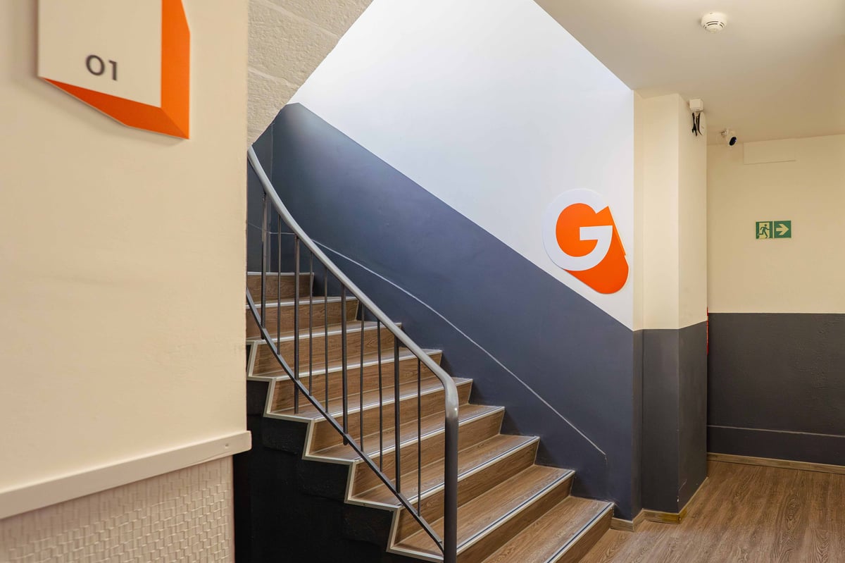 Staircase with metal railing in an easyHotel, featuring a grey wall with the orange "G" logo.