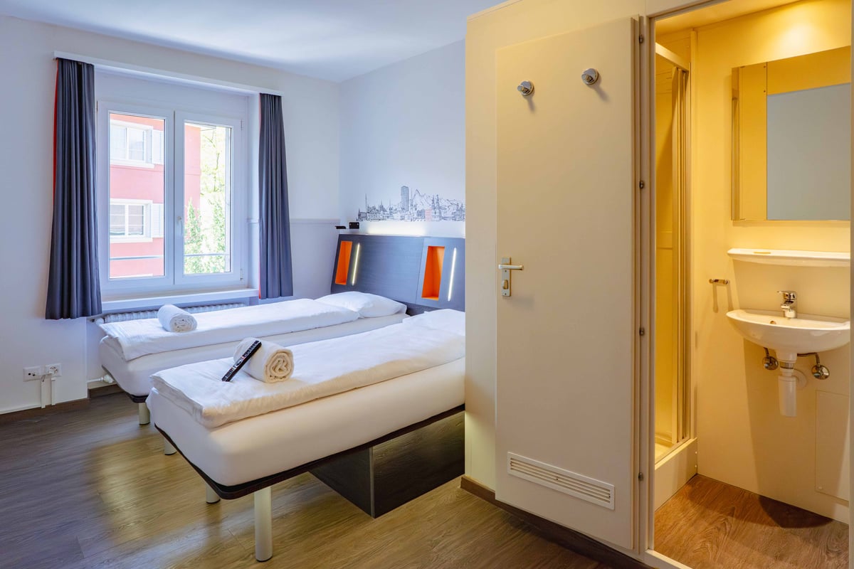 EasyHotel Zurich Limmatplatz twin room with two single beds, white linens, and a window with grey curtains.