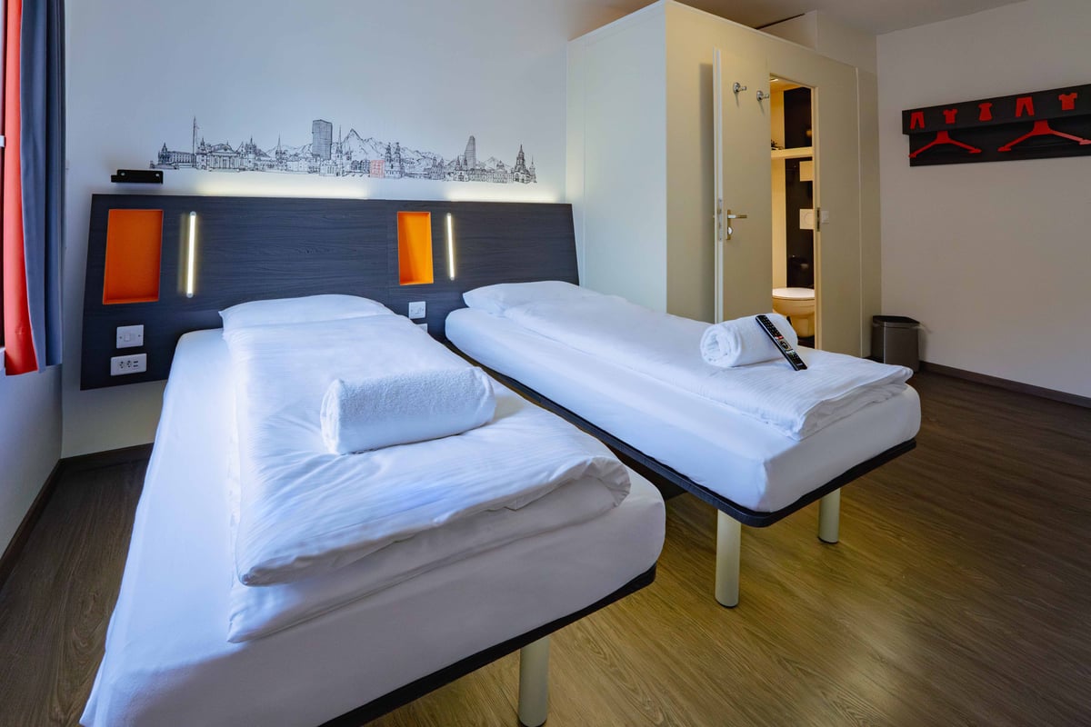 EasyHotel Zurich Limmatplatz twin room with two single beds, white linens, and a city skyline mural.