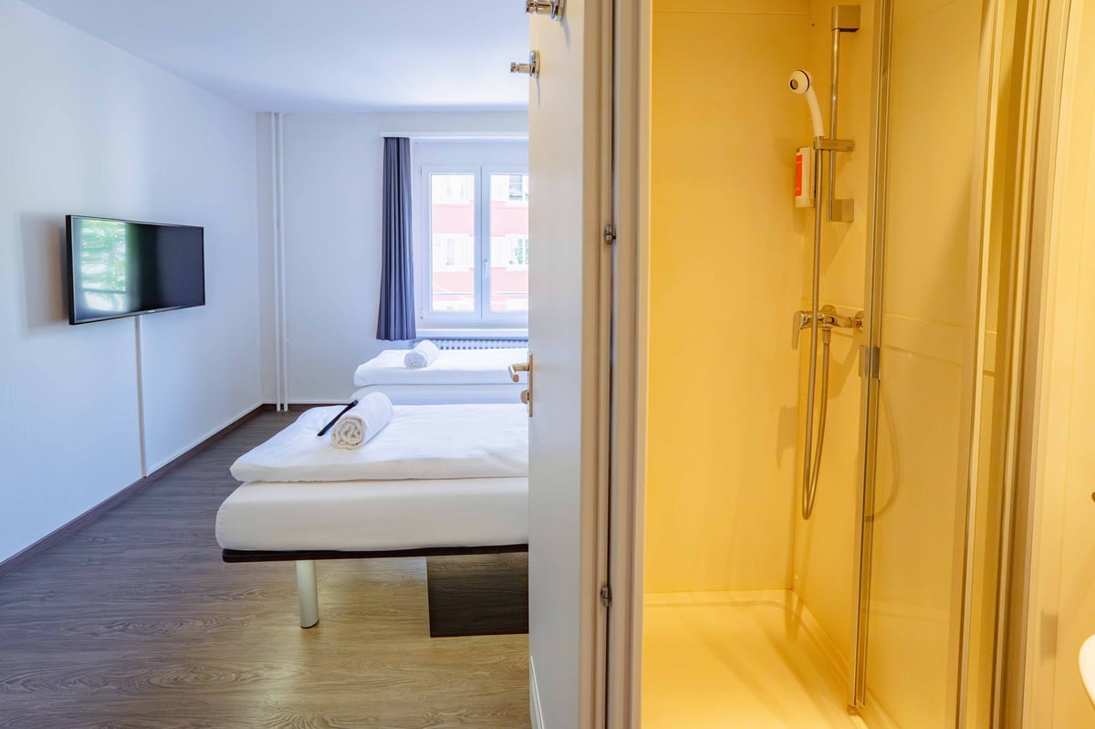 EasyHotel Zurich Limmatplatz twin room with two single beds, a wall-mounted TV, and a visible shower stall.