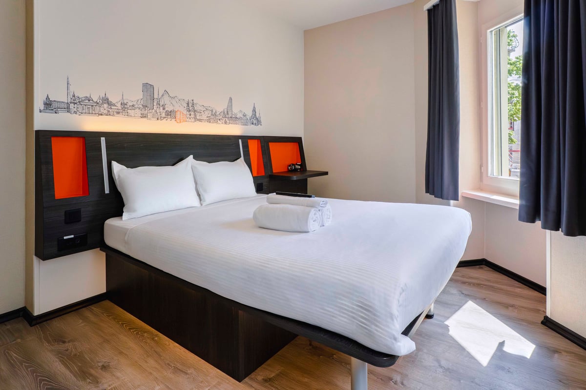 EasyHotel Zurich Main Station Double Room with bed, pillows, and city skyline wall decal.