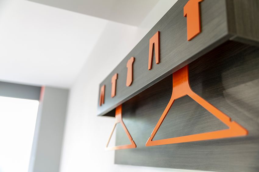 Close-up of the distinctive orange hangers and clothing icons on a dark grey wooden wall shelf in an easyHotel Reading room.