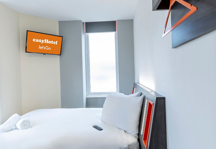 Modern easyHotel room in Reading featuring a crisp white bed, wall-mounted TV, and signature orange accents.