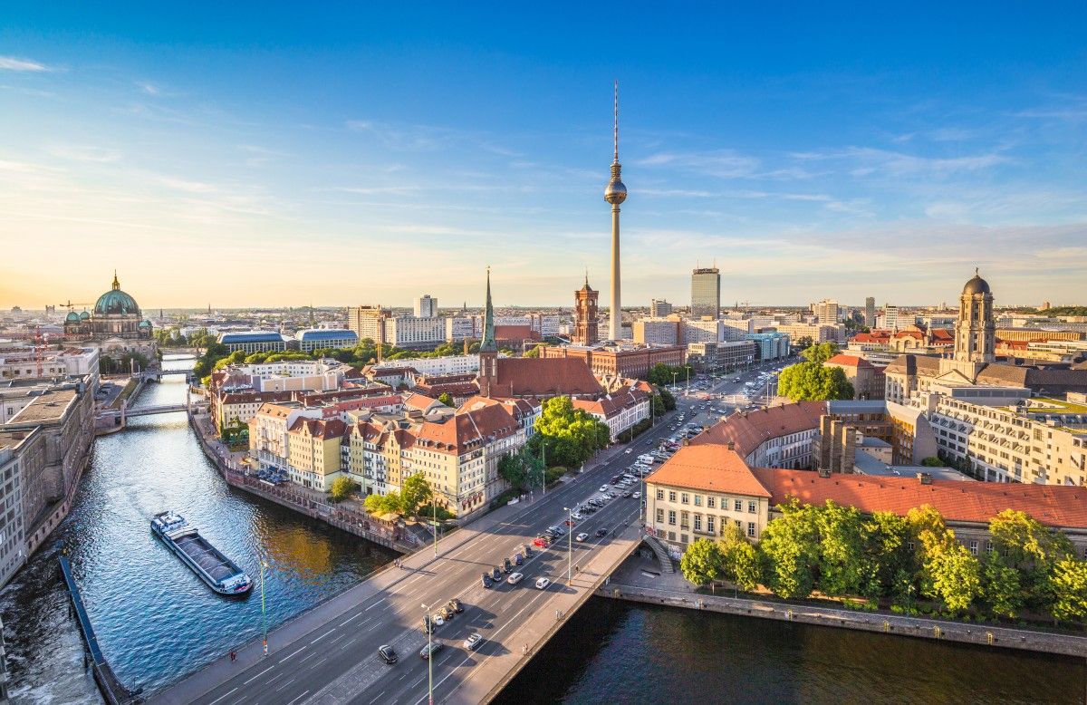 Panoramic view of Berlin, Germany, showcasing the Spree River, Berliner Dom cathedral, and the iconic Fernsehturm TV Tower against a clear blue sky.