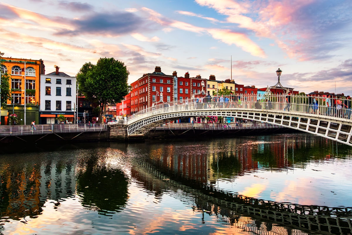 Alt text: Historic Ha'penny Bridge spanning the River Liffey in Dublin, Ireland at sunset, with colorful traditional buildings lining the riverbanks.