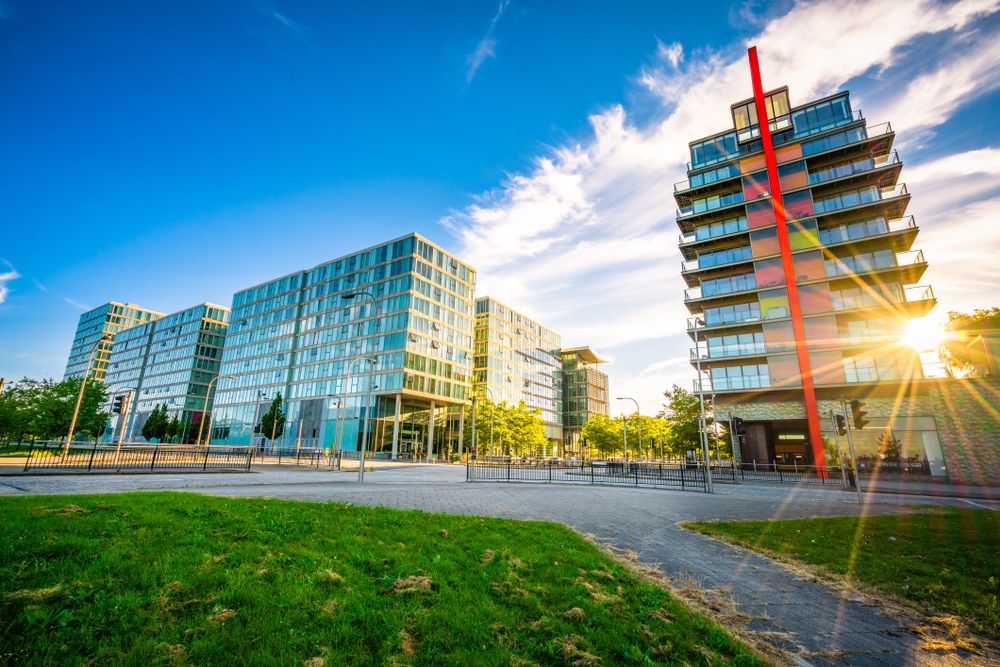 Modern architecture in Amsterdam's Amstelkwartier, featuring sleek glass buildings and a colorful tower with a prominent red stripe, under a clear blue sky.