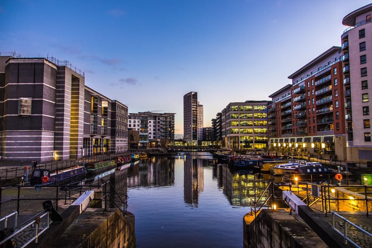 Leeds Dock canal at dusk with modern waterfront buildings, illuminated offices, and moored narrowboats, Leeds, UK.