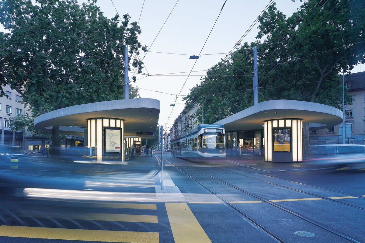 Modern tram stop at Limmatplatz, Zurich, with two curved concrete shelters, a tram, and blurred city traffic at dusk.