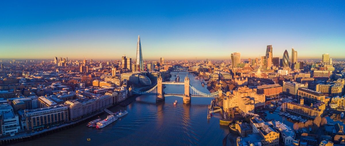 Panoramic aerial view of London, UK cityscape at sunrise, featuring Tower Bridge over the River Thames and iconic skyscrapers like The Shard.