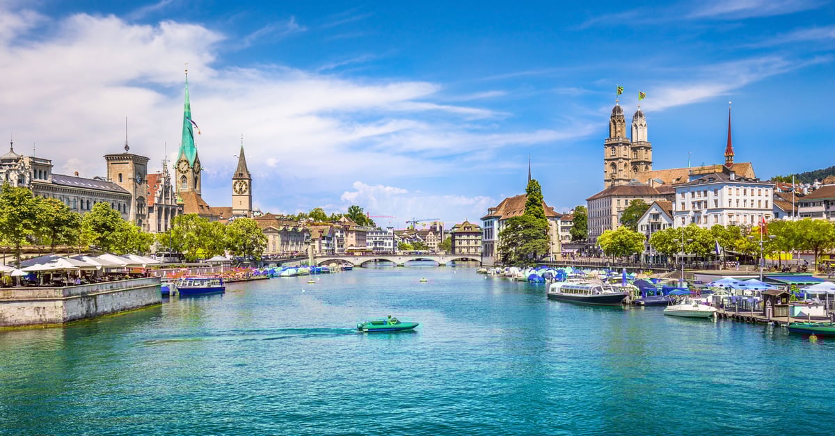 Vibrant blue river leading to Zurich Lake. The banks of the river are lined with boats, restaurants and churches. 