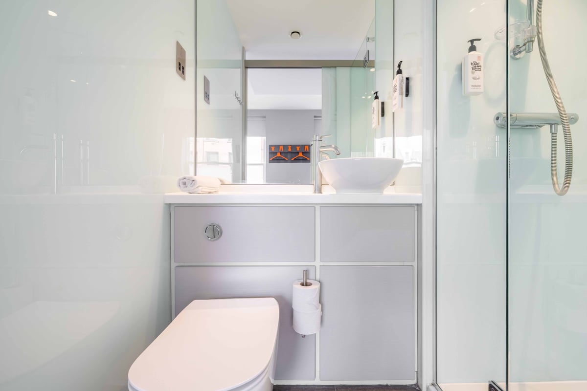 Bathroom with white toilet, sink, rolled towel, and mirrored wall.