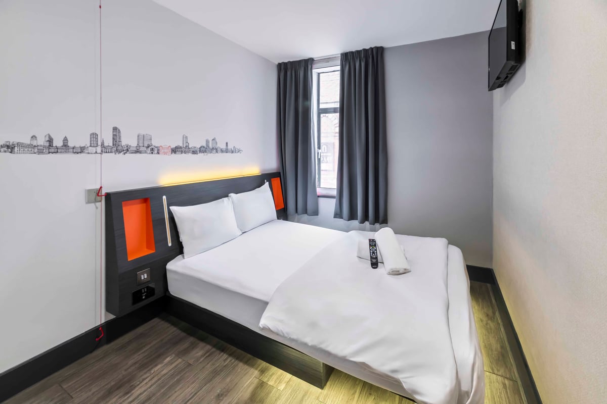 Double bed with rolled towels and a TV mounted on the wall.