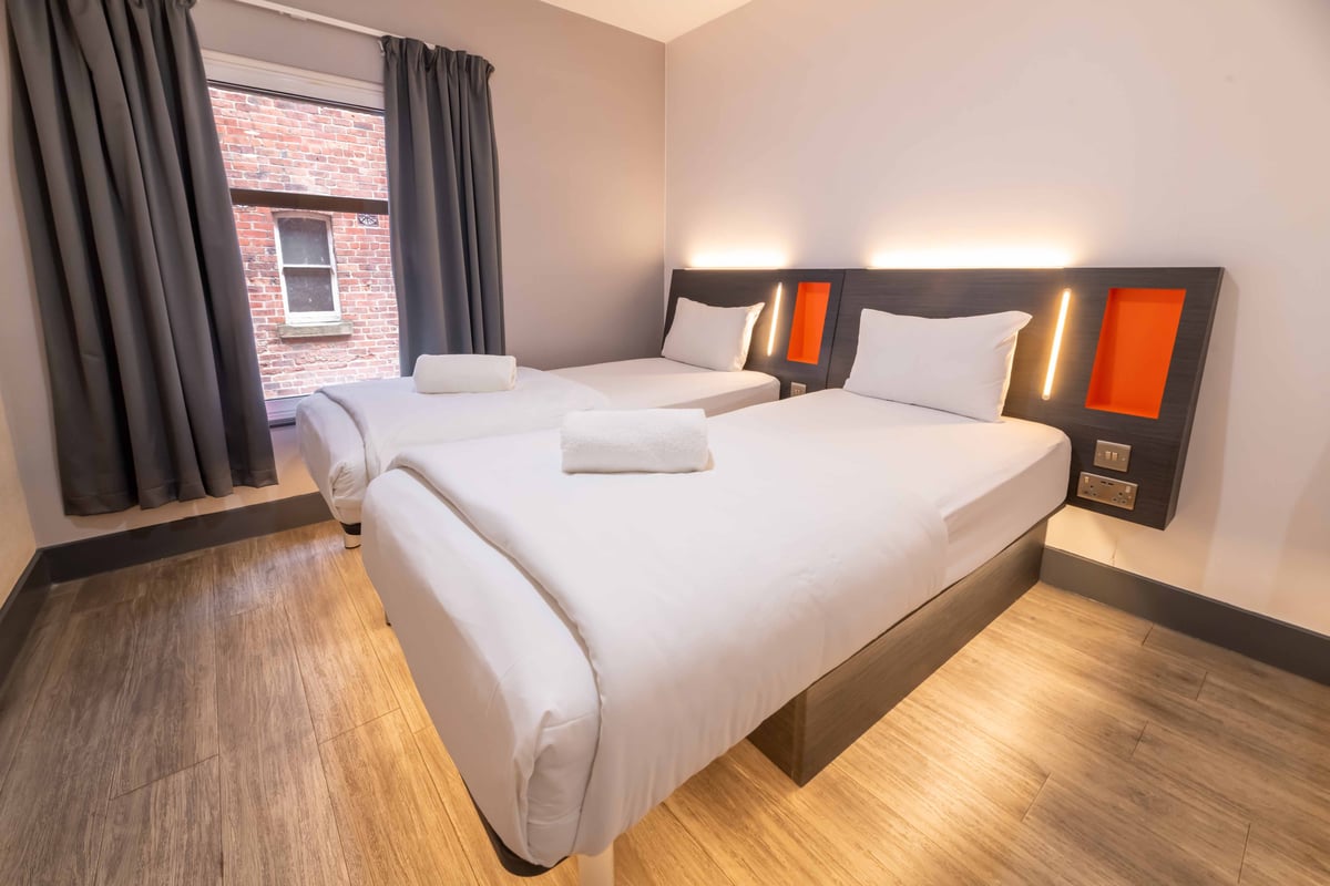 Hotel room with two beds, cityscape wall art, and towels with TV remote on the front bed.