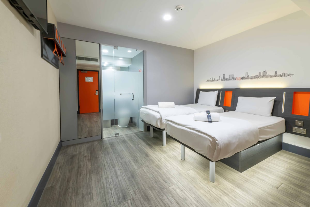 Hotel room with two single beds, frosted glass bathroom, and orange door in background.