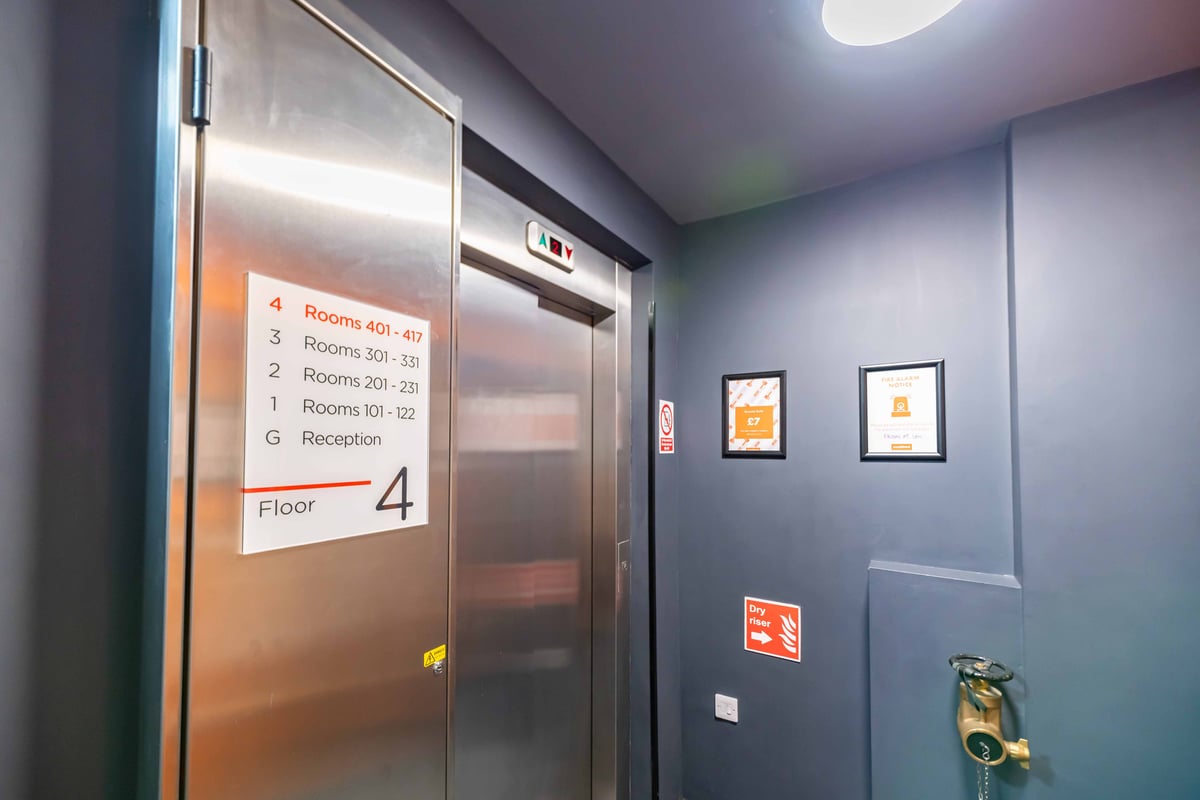 Elevator area on floor 4 with room directory, framed notices, and fire safety signage.