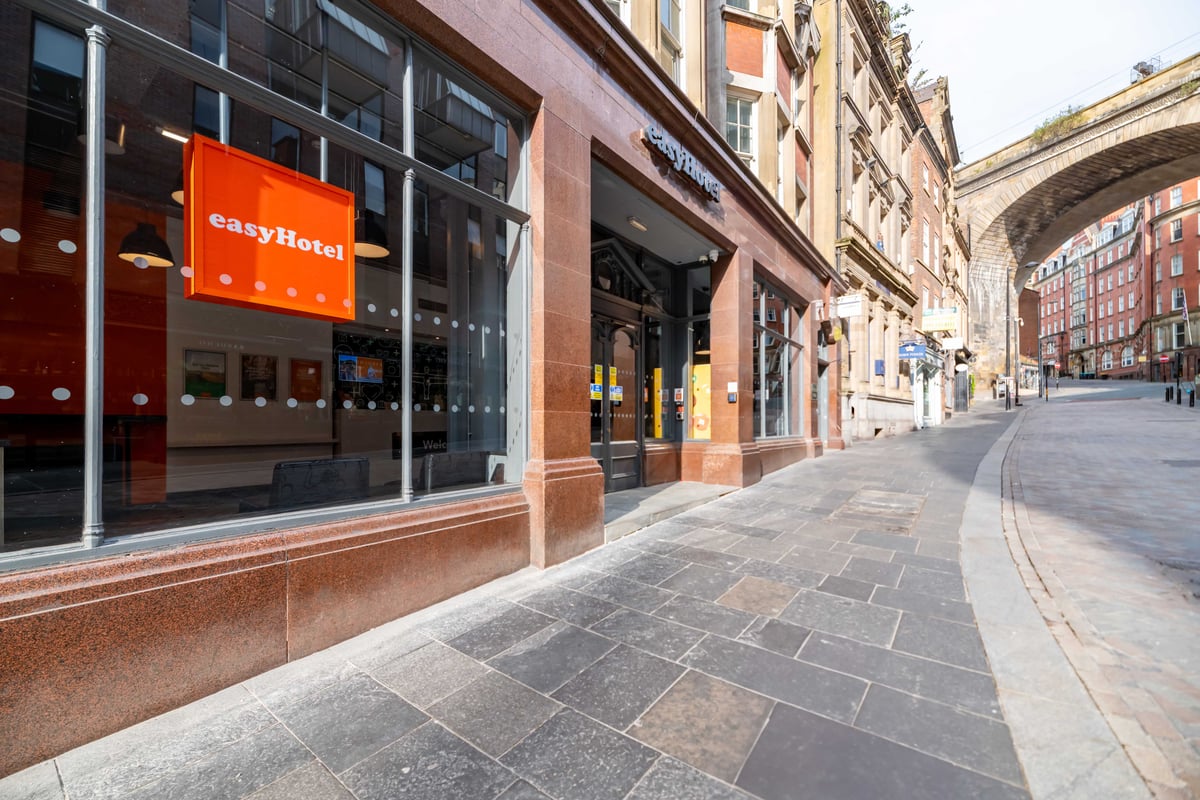Side view of easyHotel entrance with orange sign and arched bridge in background.
