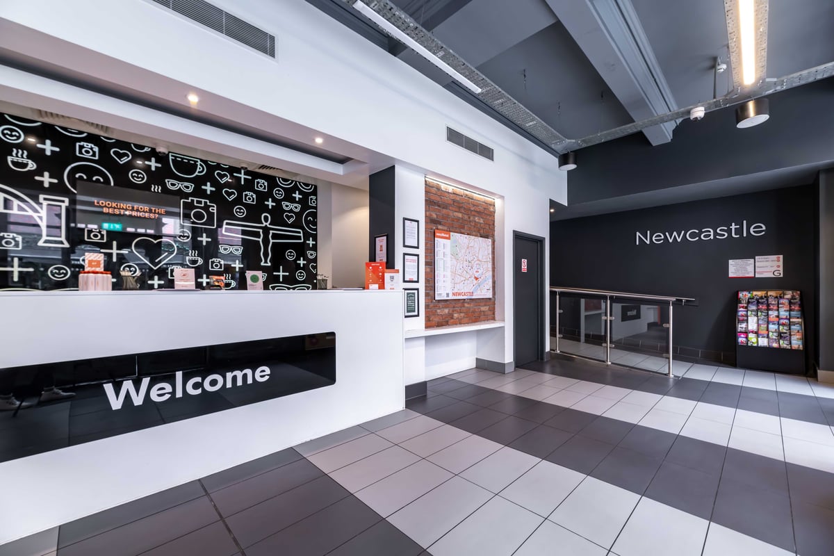 Hotel lobby with "Welcome" sign at reception desk and "Newcastle" on back wall.
