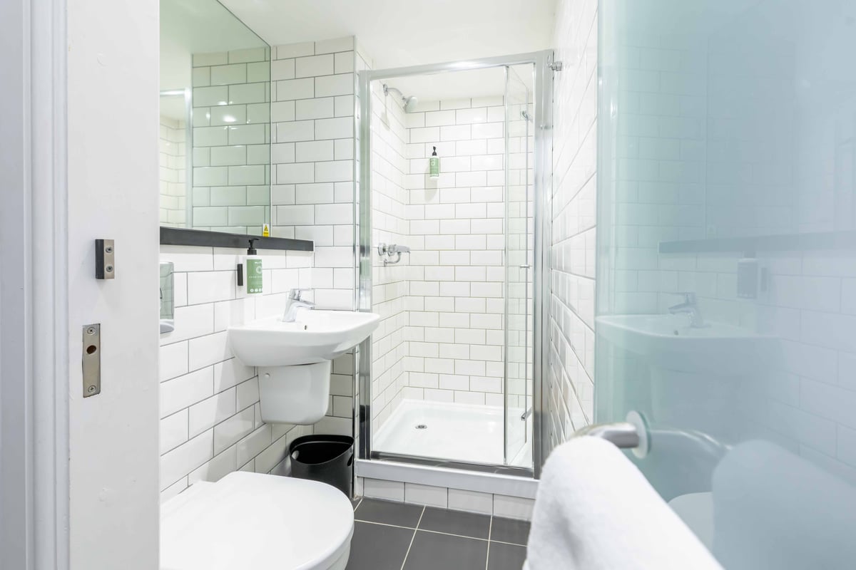 Bathroom with shower, sink, toilet, and white tile walls.