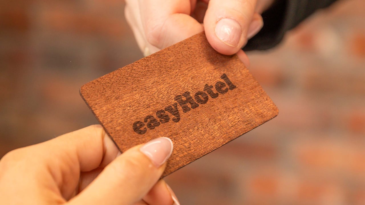 Close-up of hands exchanging a sustainable brown wooden easyHotel key card, with the easyHotel logo engraved on its surface.