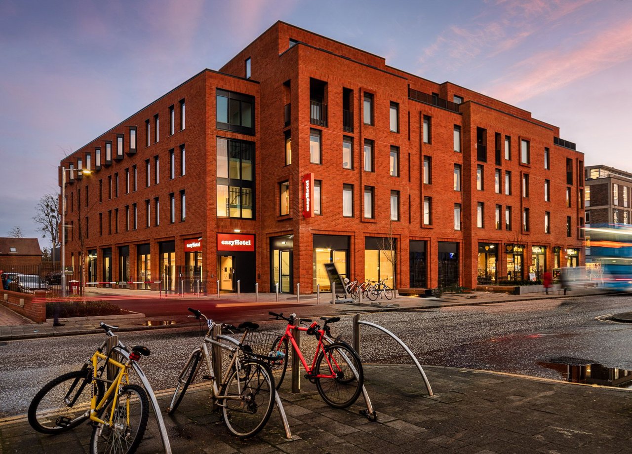 Modern easyHotel building exterior in Oxford at twilight, featuring brick architecture, large windows, and parked bicycles on the street with blurred traffic.