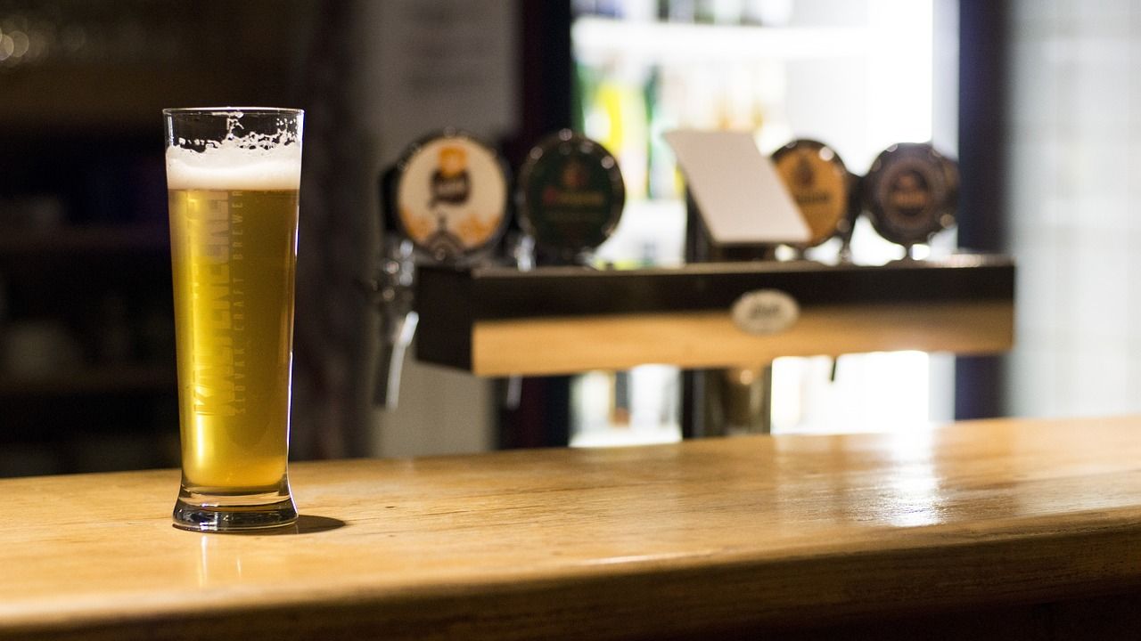 Tall glass of golden Slovenian craft beer with a foamy head on a wooden bar counter, with blurred beer taps in the background of a pub.