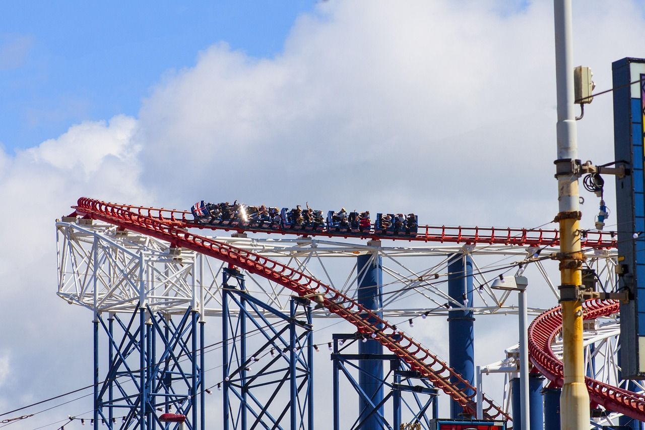 The Big One rollercoaster with riders on a red track at Blackpool Pleasure Beach under a blue sky.