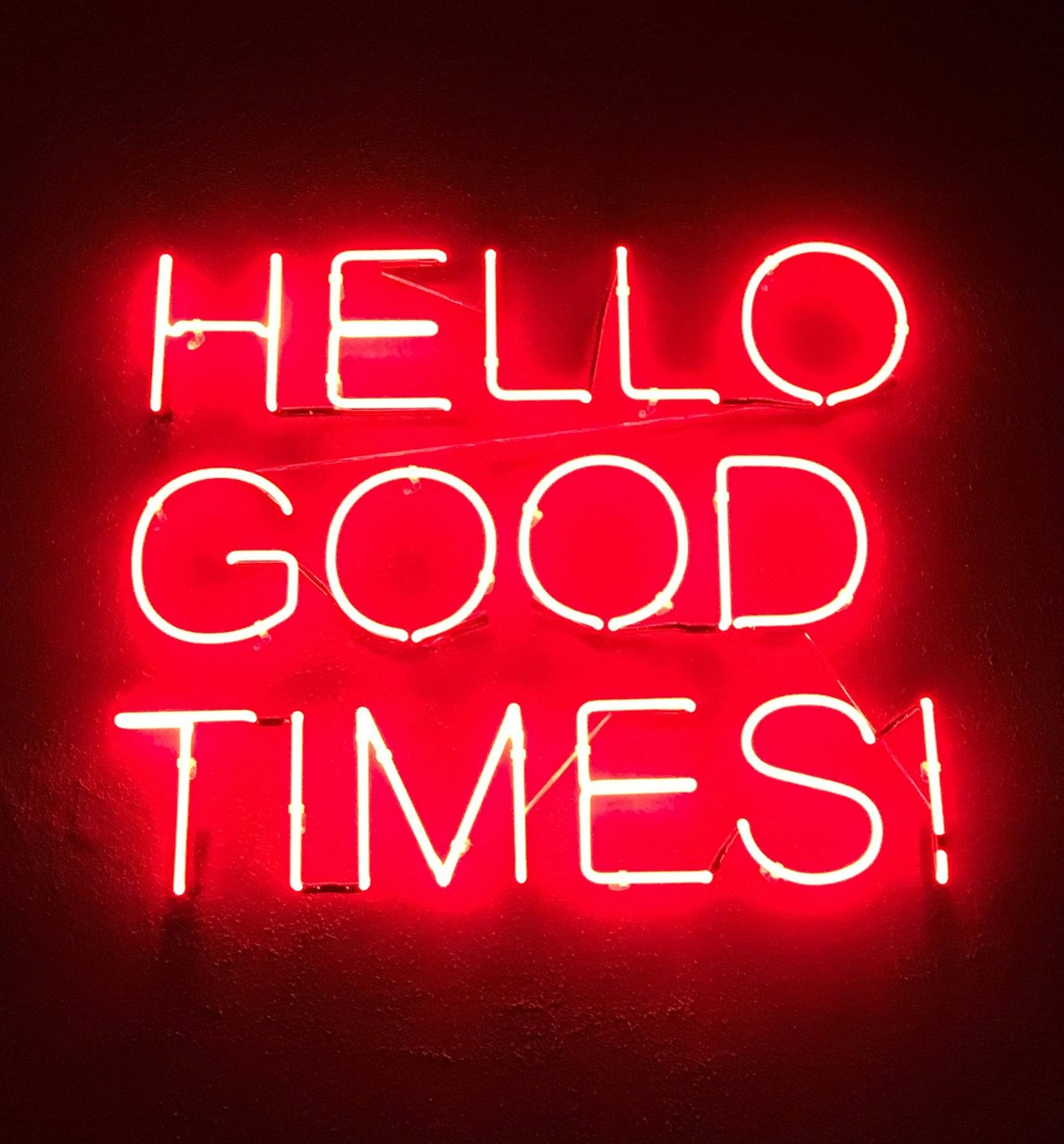 Bright red neon sign illuminating a dark background with the encouraging phrase 'HELLO GOOD TIMES!'