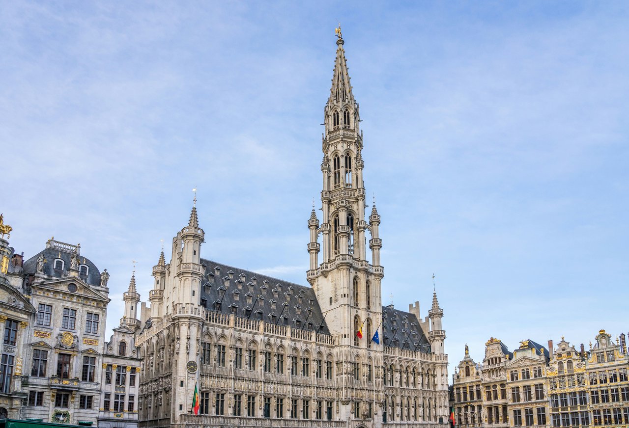 Grand Place, Brussels, Belgium. The majestic Gothic Town Hall with its towering spire and intricate facade, flanked by ornate guild houses under a bright sky.