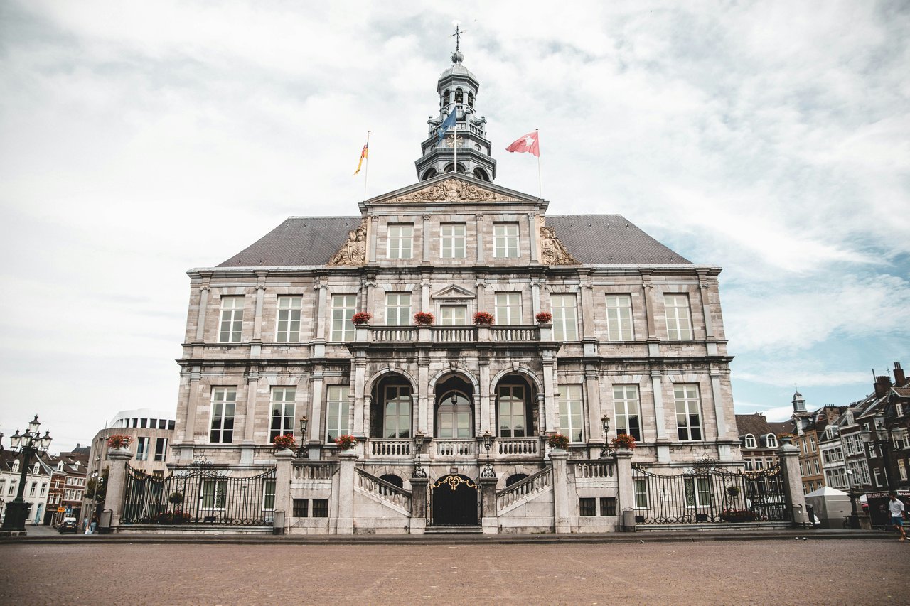 Historic Stadhuis van Maastricht, the City Hall in the Netherlands, showcasing its grand Baroque facade, elaborate stone details, iconic tower, and flags on Markt square.